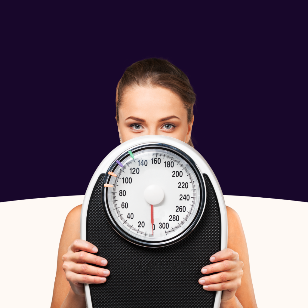 Woman peeking over a bathroom scale, highlighting the focus on numbers in weight loss.