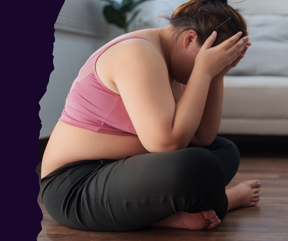 A woman sits on the floor, head in hands, appearing frustrated or upset about her body.