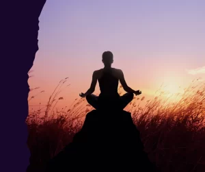 Silhouette of a woman in a meditative yoga pose on a rock at sunset, representing nervous system regulation and hormonal peace.