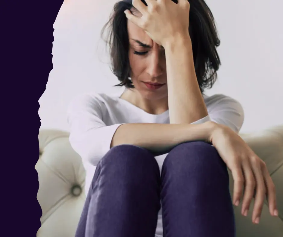 Exhausted woman sitting, holding her forehead. Visual representation of stress, overwhelm, and burnout.