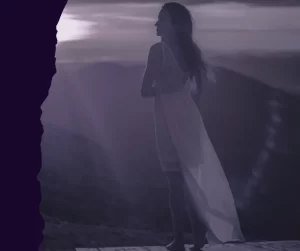 Silhouette of a woman in a white dress standing confidently on a mountain peak at sunset, symbolizing personal power and standing tall.