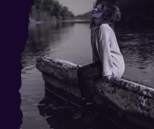 A woman sitting calmly on a stone ledge by a river, representing internal authority and the quiet power of aligned boundaries.