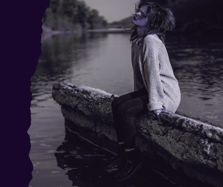 A woman sitting calmly on a stone ledge by a river, representing internal authority and the quiet power of aligned boundaries.