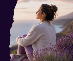 Woman resting peacefully by the ocean surrounded by purple flowers, representing support, healing, and women’s health.